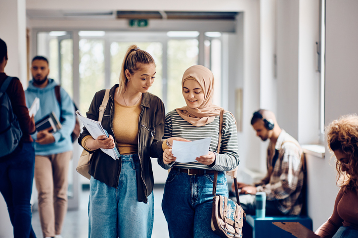 Twee studenten lopen op op school. Ze zijn met elkaar in gesprek.