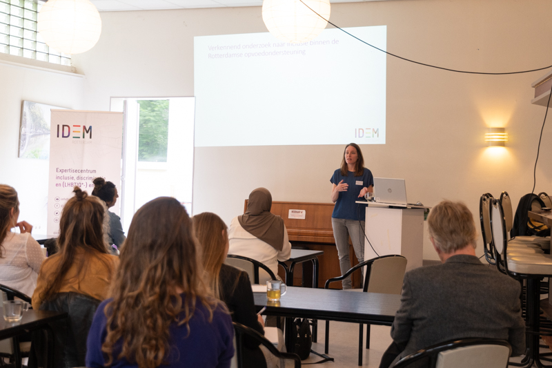 Twee personen spreken voor een zaal met publiek voor een projectiescherm.