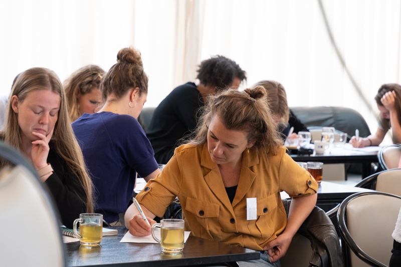 Er zitten personen aan tafels te schrijven.