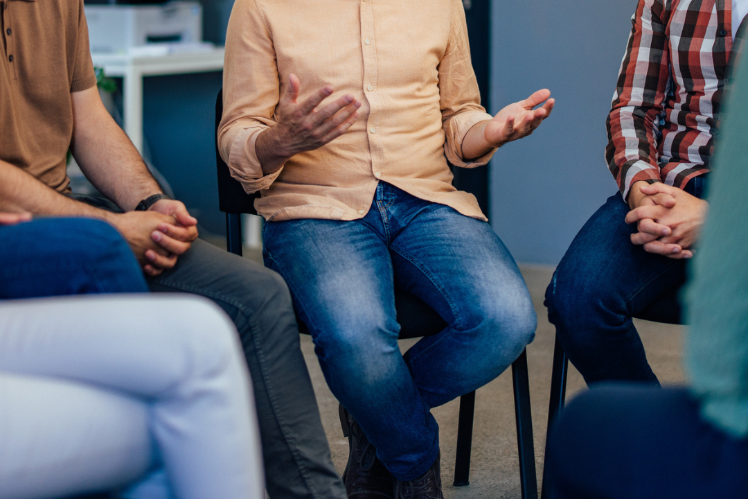 Mannen zitten in een kring op stoelen en zijn met elkaar in gesprek.