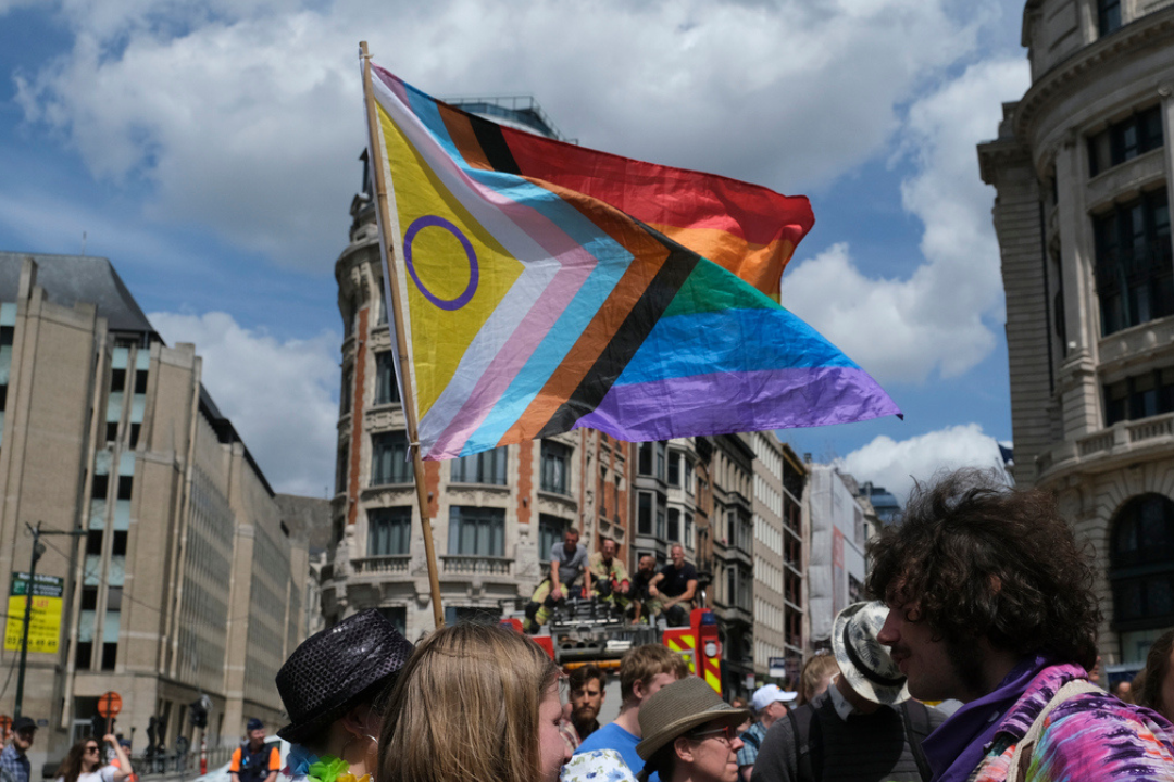 Progress Pride-vlag wappert in de wind en wordt omhoog gehouden door een groep jonge mensen.