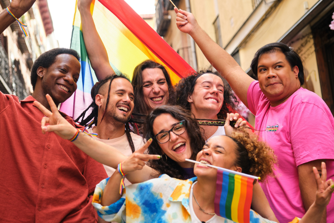 Blij gezelschap van lhbtqia+-personen die lachen en glimlachen met regenboogvlaggen.
